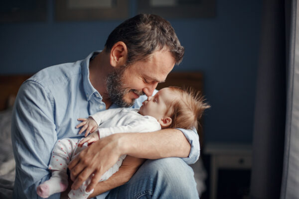 Middle age Caucasian father kissing sleeping newborn baby girl. Parent holding rocking child daughter son in hands. Authentic lifestyle parenting fatherhood moment. Single dad family home life.