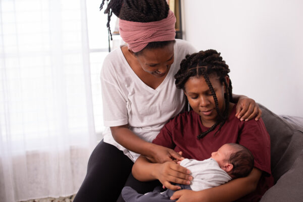 Lovely lesbian couple with their baby. Happy friends sitting together on the couch.